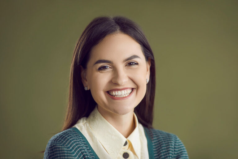 Studio close up portrait of happy smiling good looking woman. Closeup headshot of cheerful confident young girl in smart casual outfit, with pretty face and charming natural smile on green background