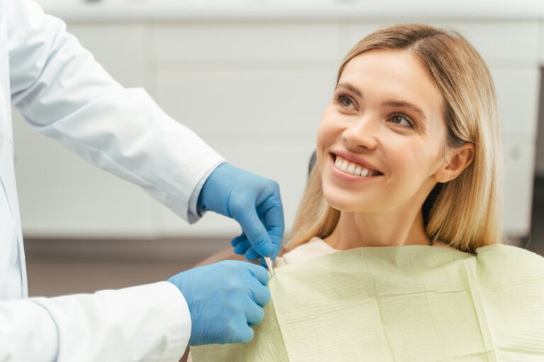 Portrait of smiling beautiful female patient with blond hair sitting in dental chair. Attractive young woman visiting modern clinic. ?oncept of dental care