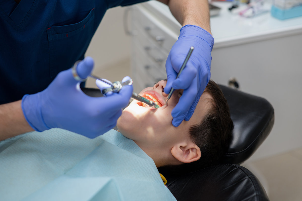 The dentist gives an anesthetic injection into the gum to a boy who is sitting in a dental chair. Dental treatment.