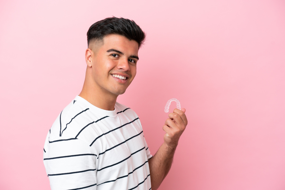 Young caucasian man holding invisaling isolated on pink background smiling a lot