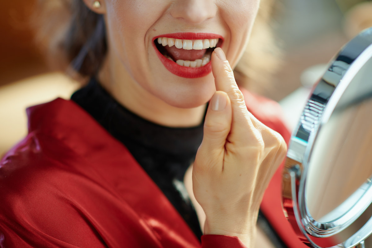 Closeup on woman in the living room in sunny day looking in mirror and checking teeth.